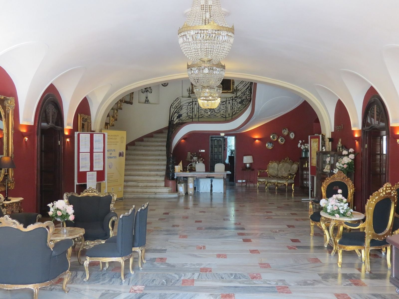 Sklepiony hol wejściowy z kryształowym żyrandolem, krętymi schodami i pozłacanymi fotelami.