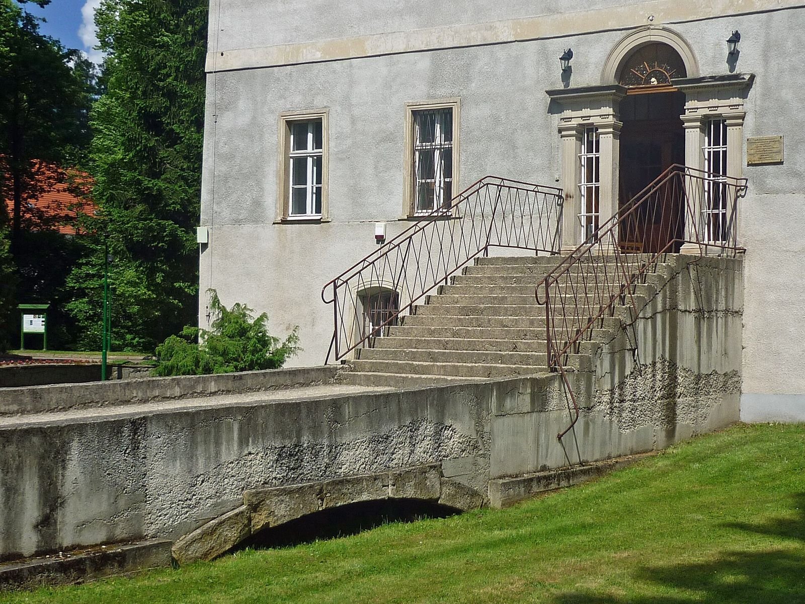 Schody z metalową balustradą prowadzące do portalu wejściowego pałacu w Bukowcu, pod nimi niski kamienny mostek.