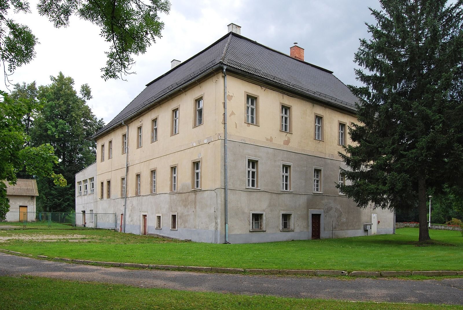 Pałac w Bukowcu od strony północno-wschodniej, widok z alejki na dwukondygnacyjną bryłę z wysokim dachem.
