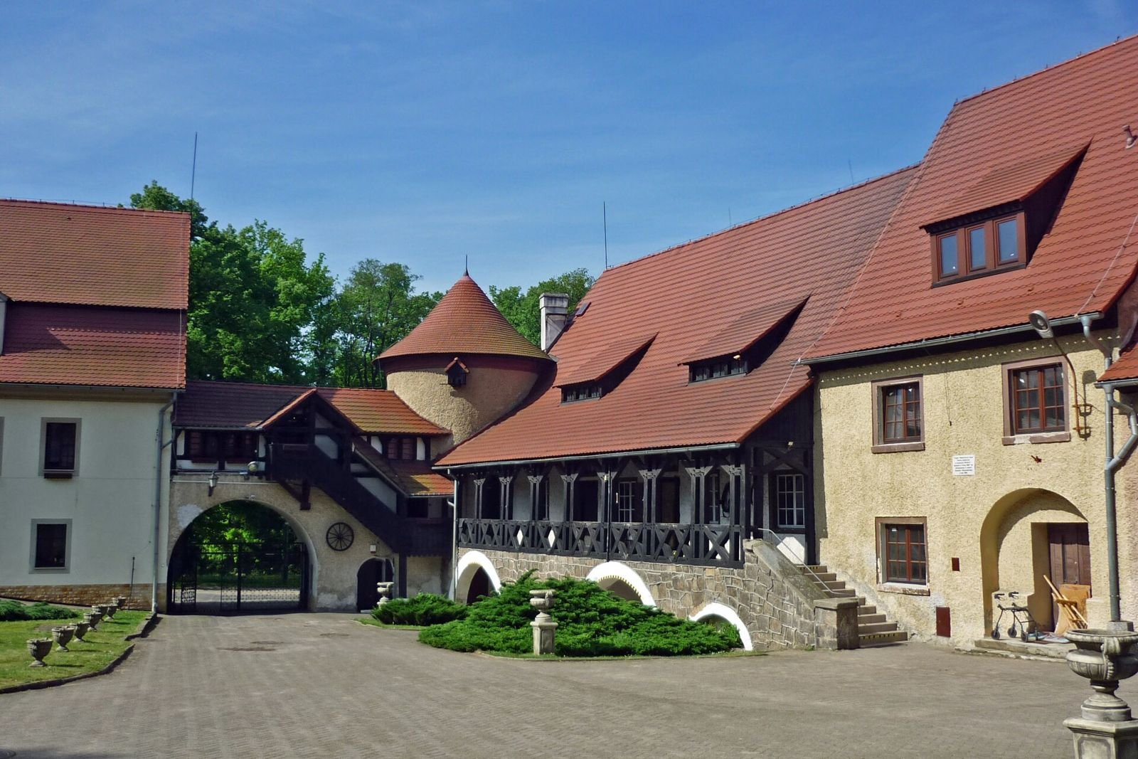 Dziedziniec zespołu pałacowego z okrągłą wieżyczką, bramą i budynkiem z drewnianą galerią.