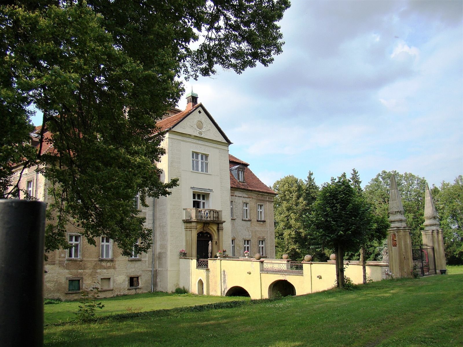 Pałac w Jastrowcu z ryzalitem, kamiennym mostem nad dawną fosą i obeliskami przy wejściu.