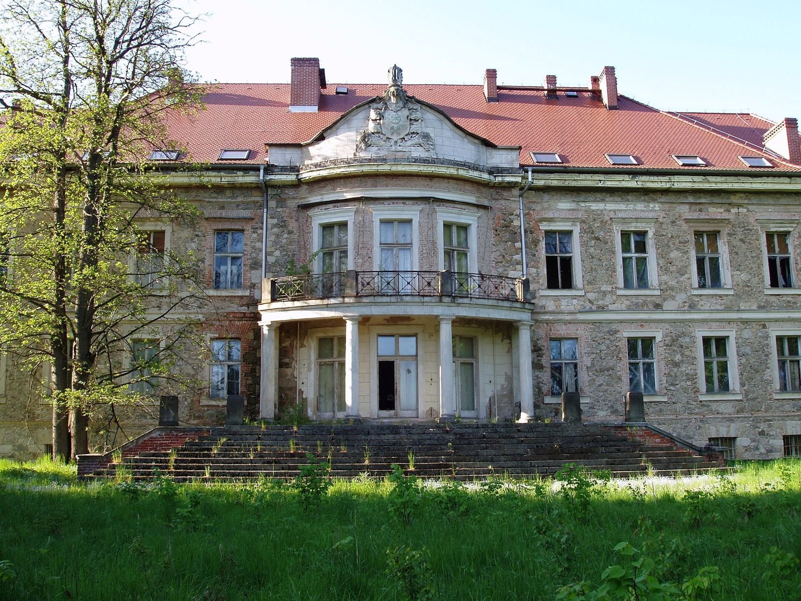 Pałac w Maciejowcu widziany od frontu: środkowy ryzalit z balkonem na kolumnach, schody i czerwony dach.