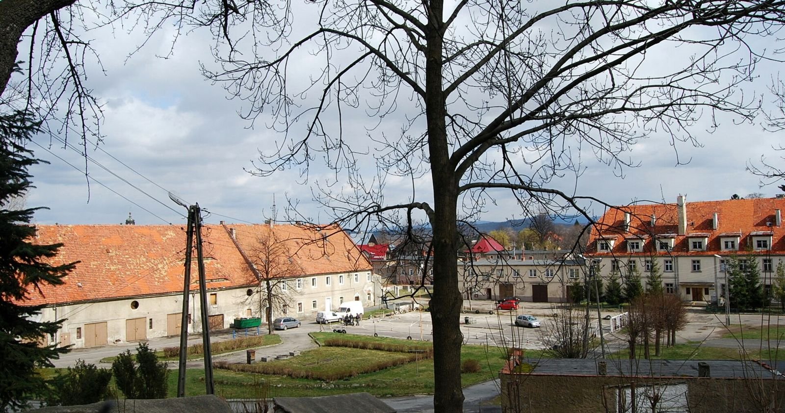 Widok z góry na dziedziniec gospodarczy z dawnymi zabudowaniami folwarku o czerwonych dachach, w tle góry.