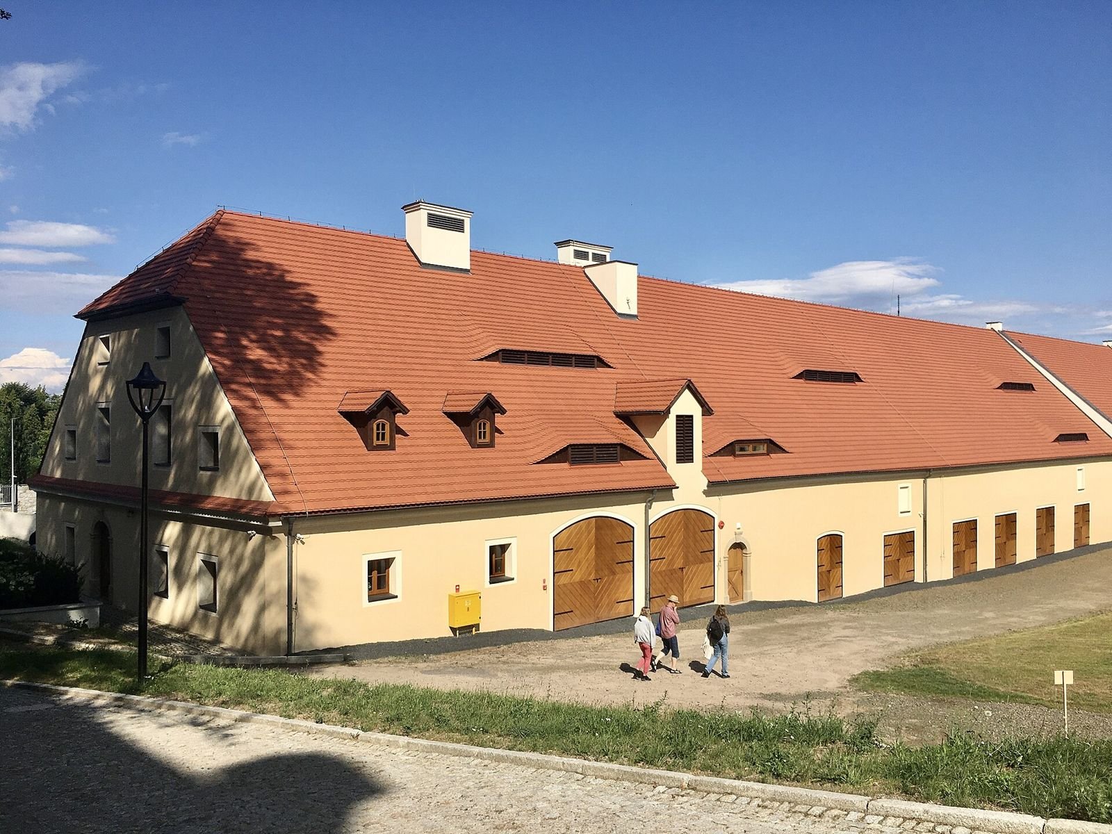 Dawna stajnia przy pałacu w Sobieszowie: długi budynek z czerwonym dachem, lukarnami i drewnianymi bramami.