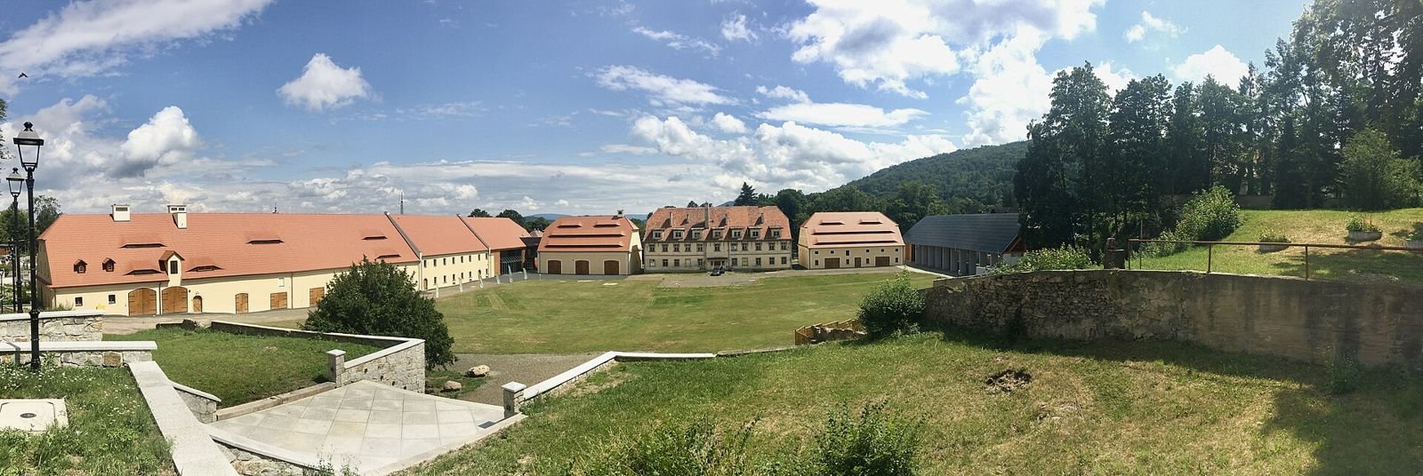 Panorama zespołu zabudowy w Sobieszowie z czerwonymi dachami, trawnikiem i zalesionym wzgórzem w tle.