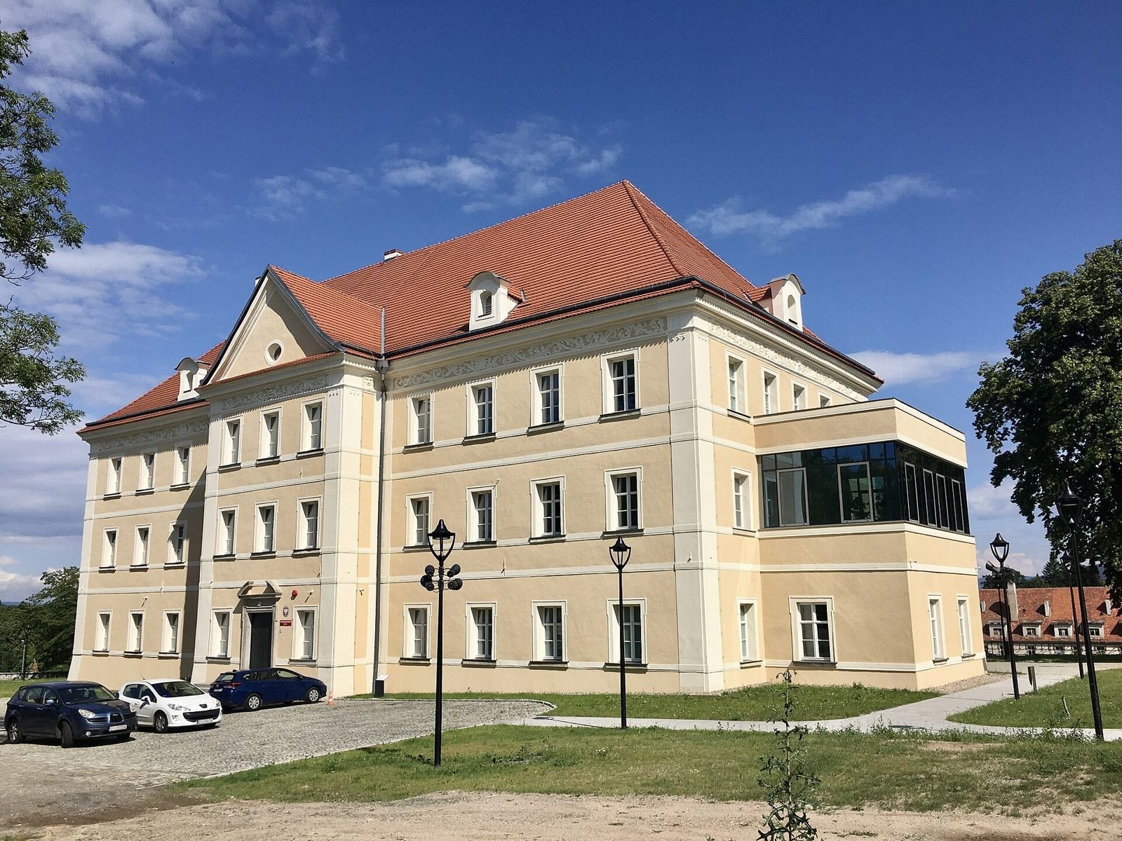 Pałac w Sobieszowie od strony wejścia: trzykondygnacyjny budynek z czerwonym dachem, jasną elewacją i przeszkloną przybudówką.