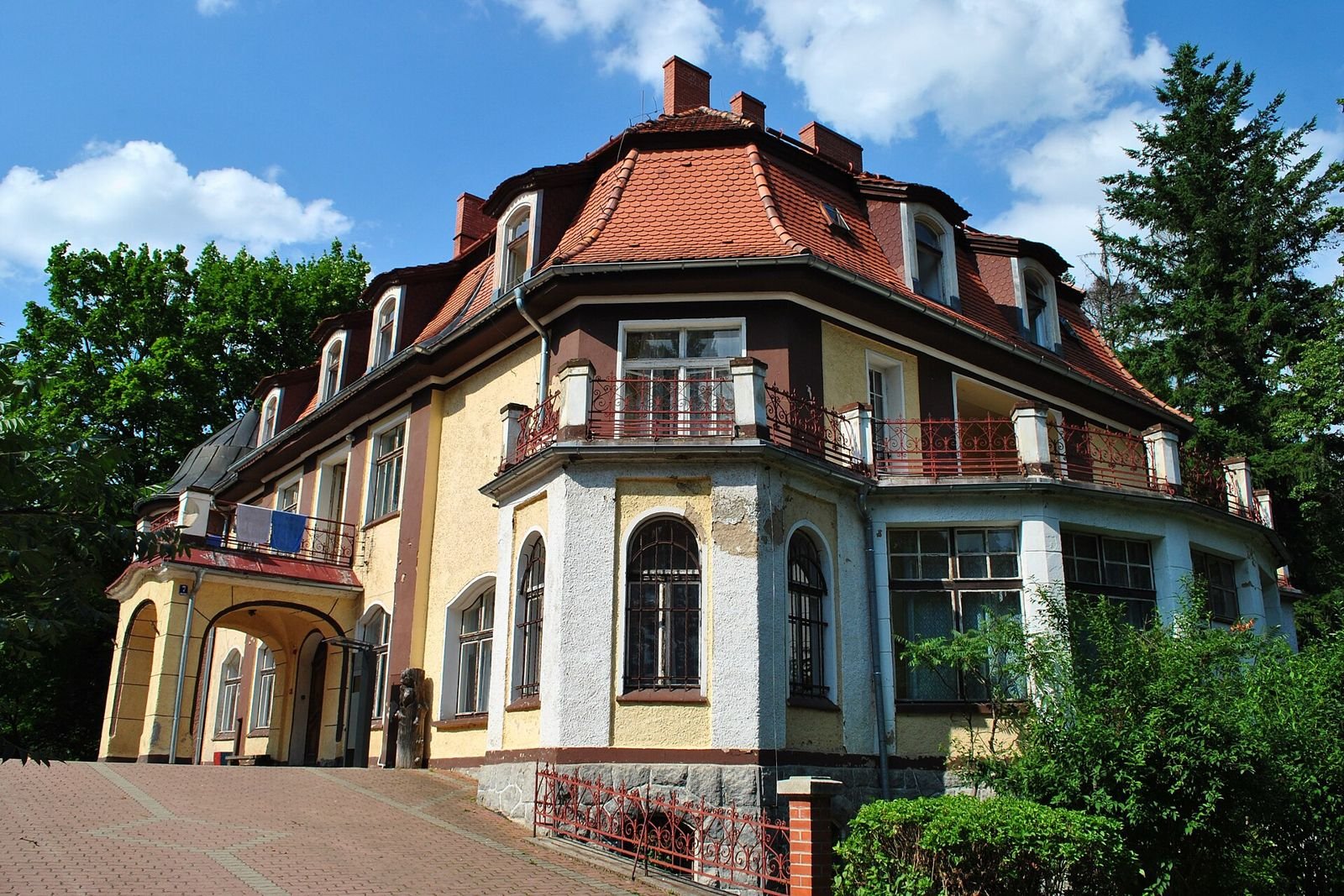 Narożnik pałacu w Muchowie z dachem mansardowym, balkonem i podcieniem wejścia.