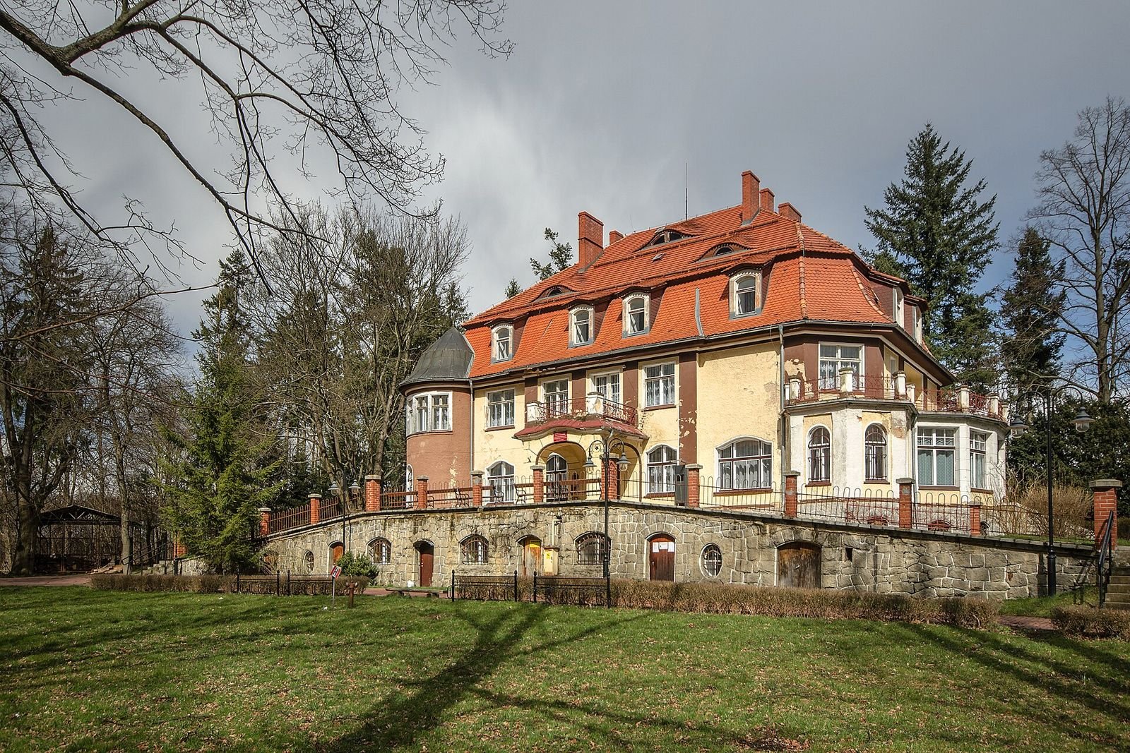 Pałac w Muchowie na tle drzew parkowych, widziany z trawnika na wzniesieniu.