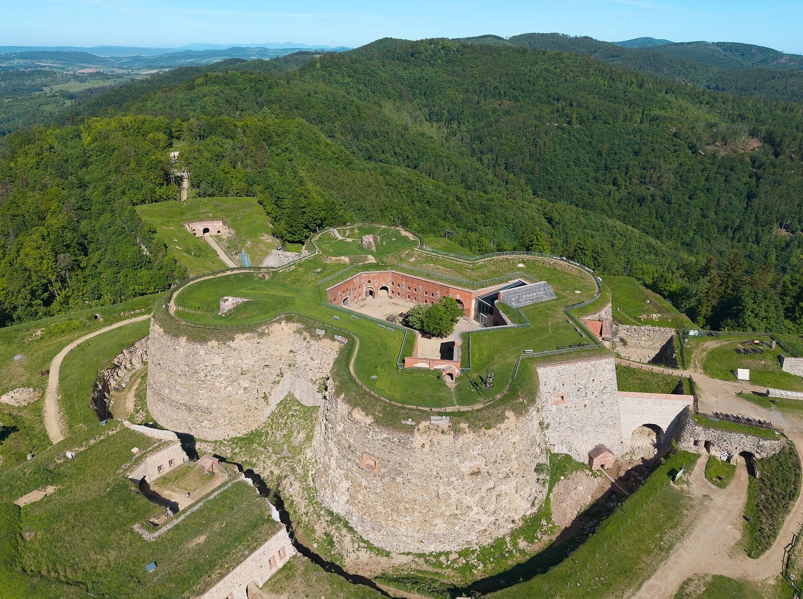 Fort główny (Donżon) Twierdzy Srebrna Góra z lotu ptaka: okrągłe kamienne wieże, trawiasta korona i ceglany dziedziniec w środku.