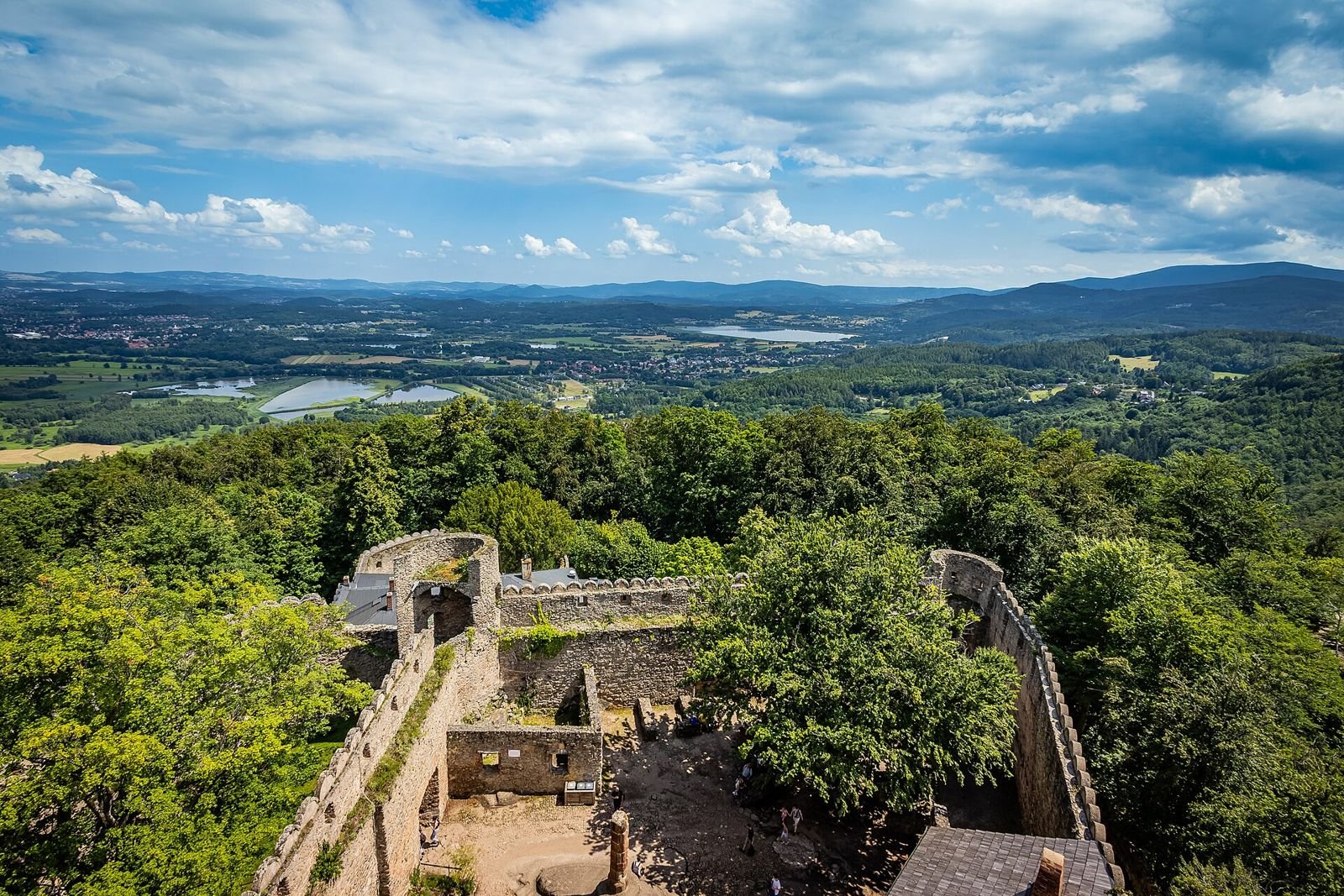 Widok z wieży Zamku Chojnik na dziedziniec ruin, otaczający las i okolicę aż po góry na horyzoncie.