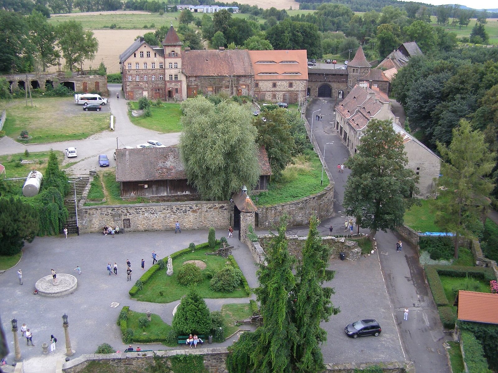 Widok z wieży Zamku Czocha na dziedziniec z klombem i fontanną oraz zabudowania przedzamcza.