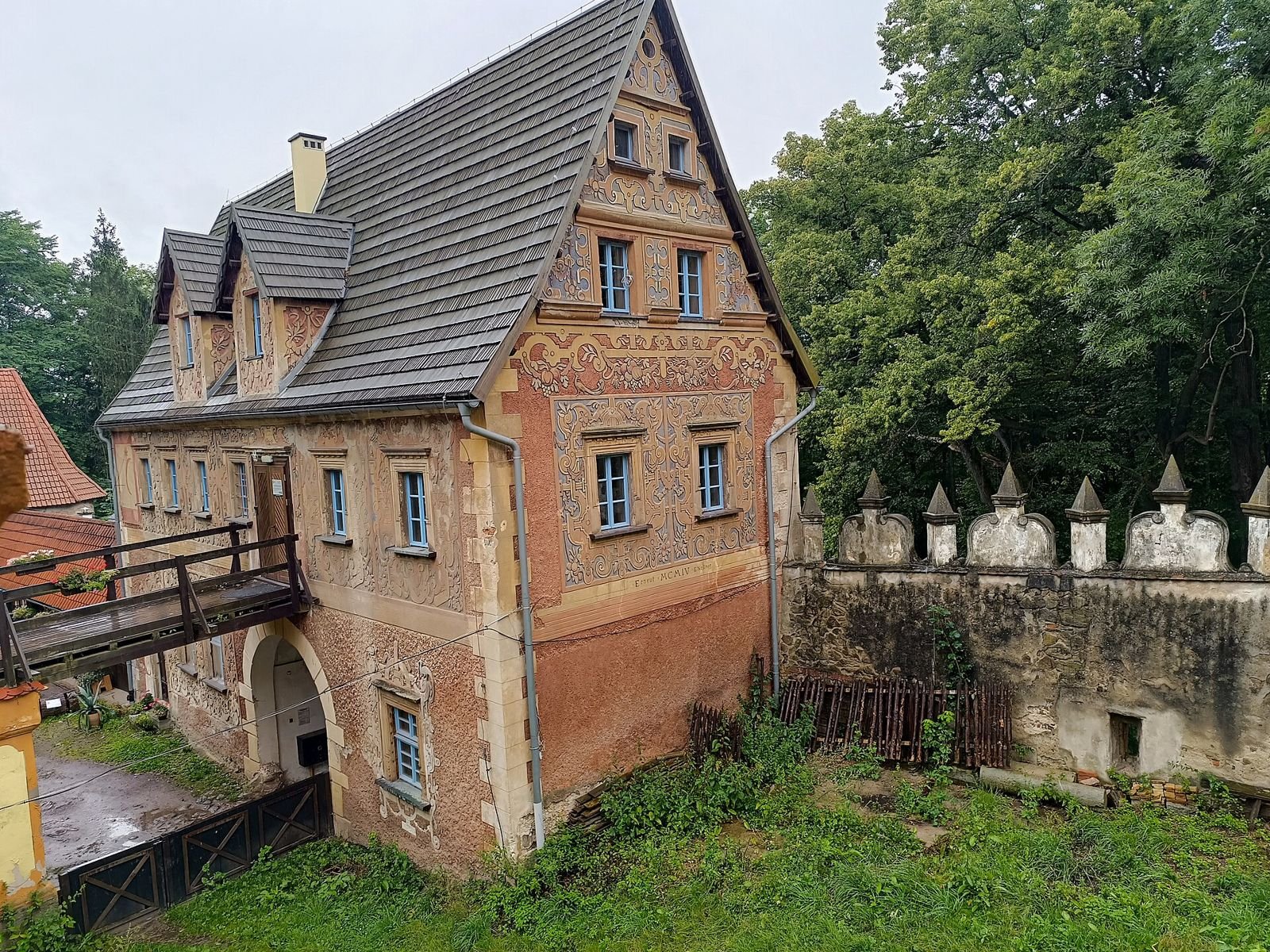 Budynek zamku Grodno z bogato zdobioną elewacją i stromym dachem, obok mur z ozdobnym zwieńczeniem.