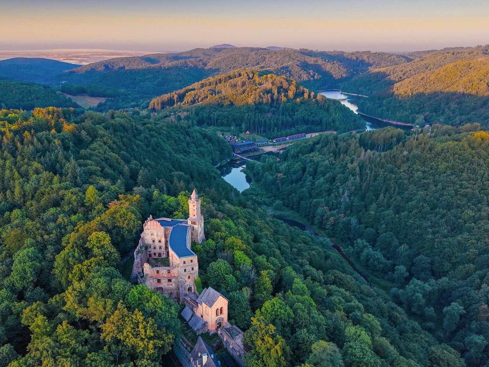Zamek Grodno z wieżą na zalesionym wzgórzu, w tle jezioro w dolinie i góry, widok z lotu ptaka.