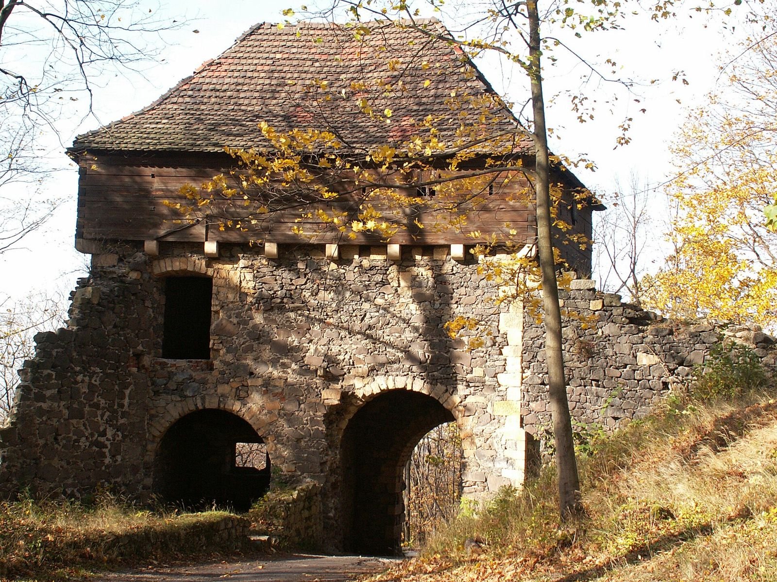 Kamienny budynek pierwszej bramy zamku Grodziec z drewnianą nadbudową i dachem z dachówki, w jesiennym słońcu.