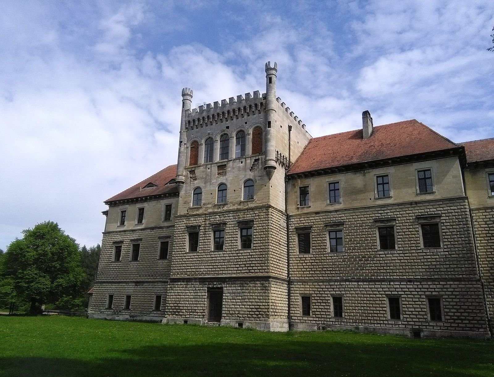Centralny ryzalit pałacu w Książu Wielkim z nadbudową z krenelażem i wieżyczkami, na tle rustykowanej elewacji.
