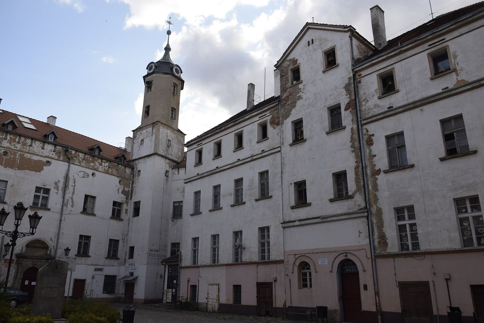 Dziedziniec zamku w Jaworze z wieżą zegarową i wysokimi, odrapanymi skrzydłami budynku.