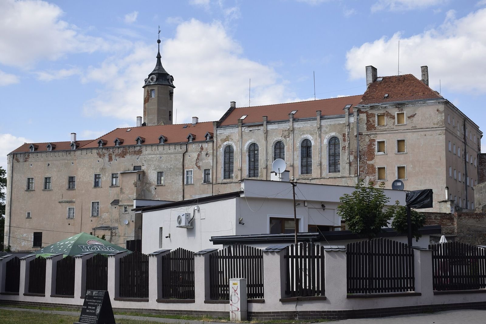 Zamek w Jaworze od strony ulicy: długa elewacja z wysokimi oknami i wieżyczką, na pierwszym planie ogrodzenie.