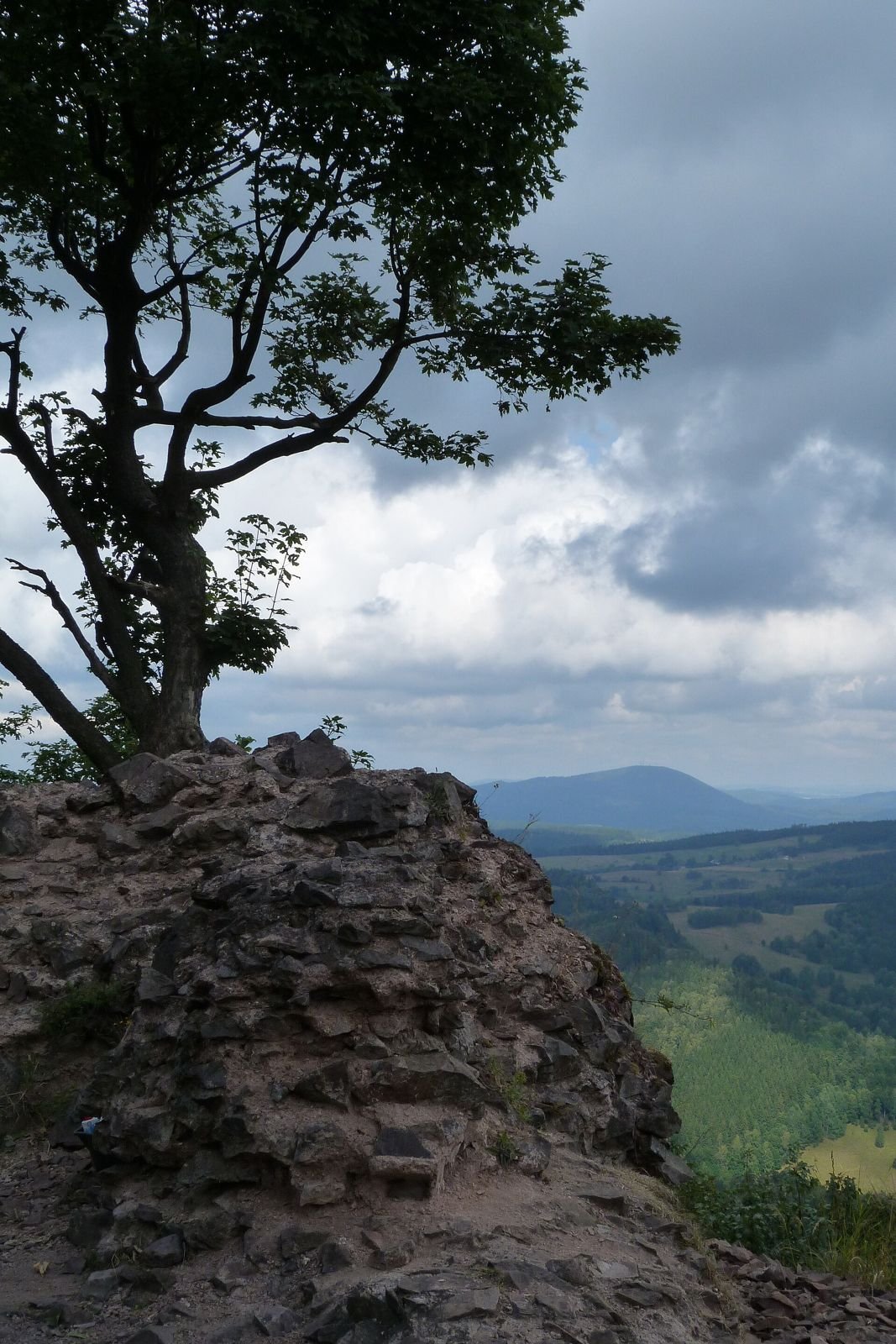 Fragment muru ruin zamku Rogowiec na tle doliny i dalekiego pasma wzgórz.