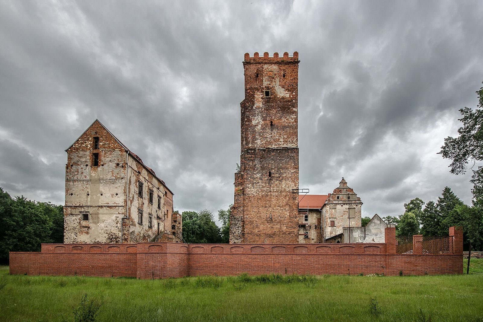 Zamek w Prochowicach z zewnątrz: ceglana wieża i budynki za niskim ceglanym murem.
