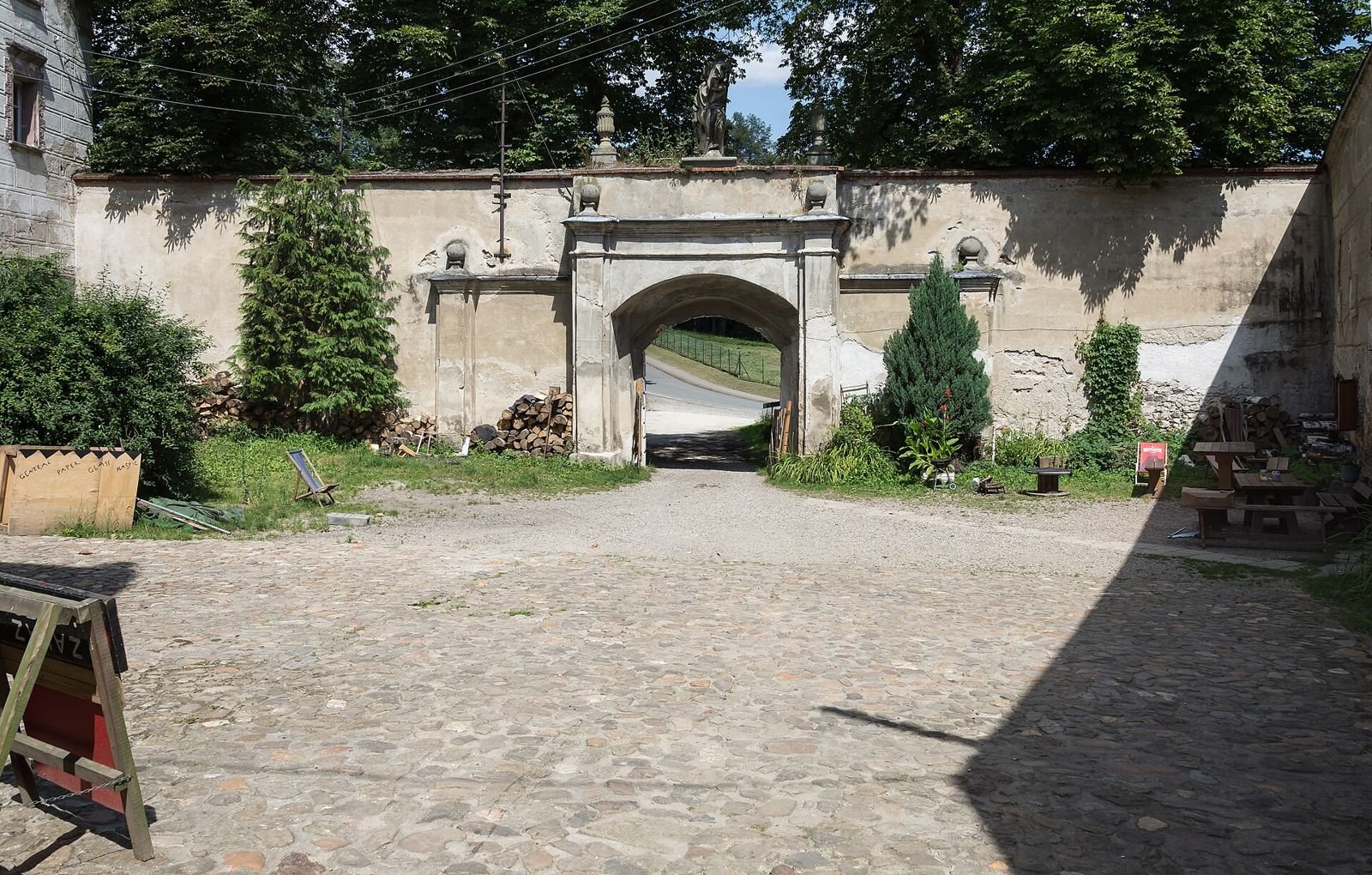 Bruk dziedzińca i mur kurtynowy z barokową bramą wejściową, za nią droga.