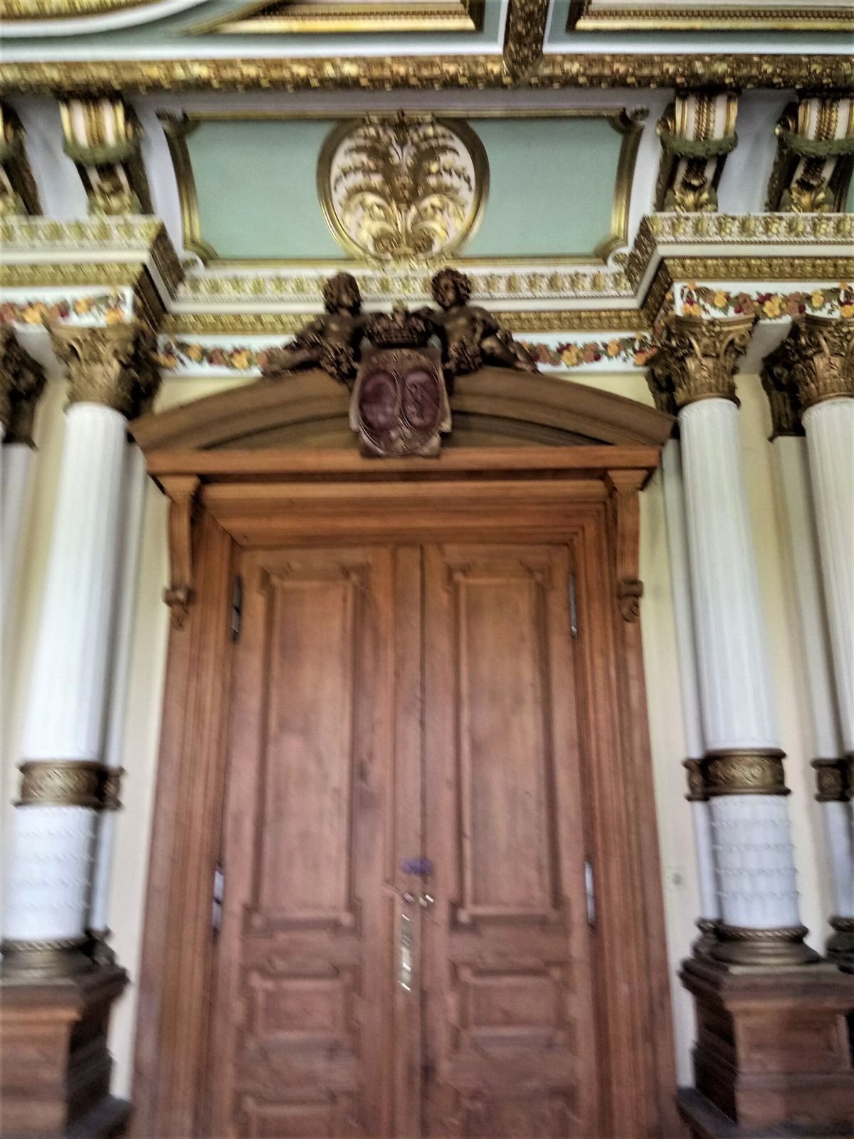 Wnętrze pałacu w Roztoce: drewniane dwuskrzydłowe drzwi we wnęce ze zdobionymi kolumnami i złoconym wykończeniem.