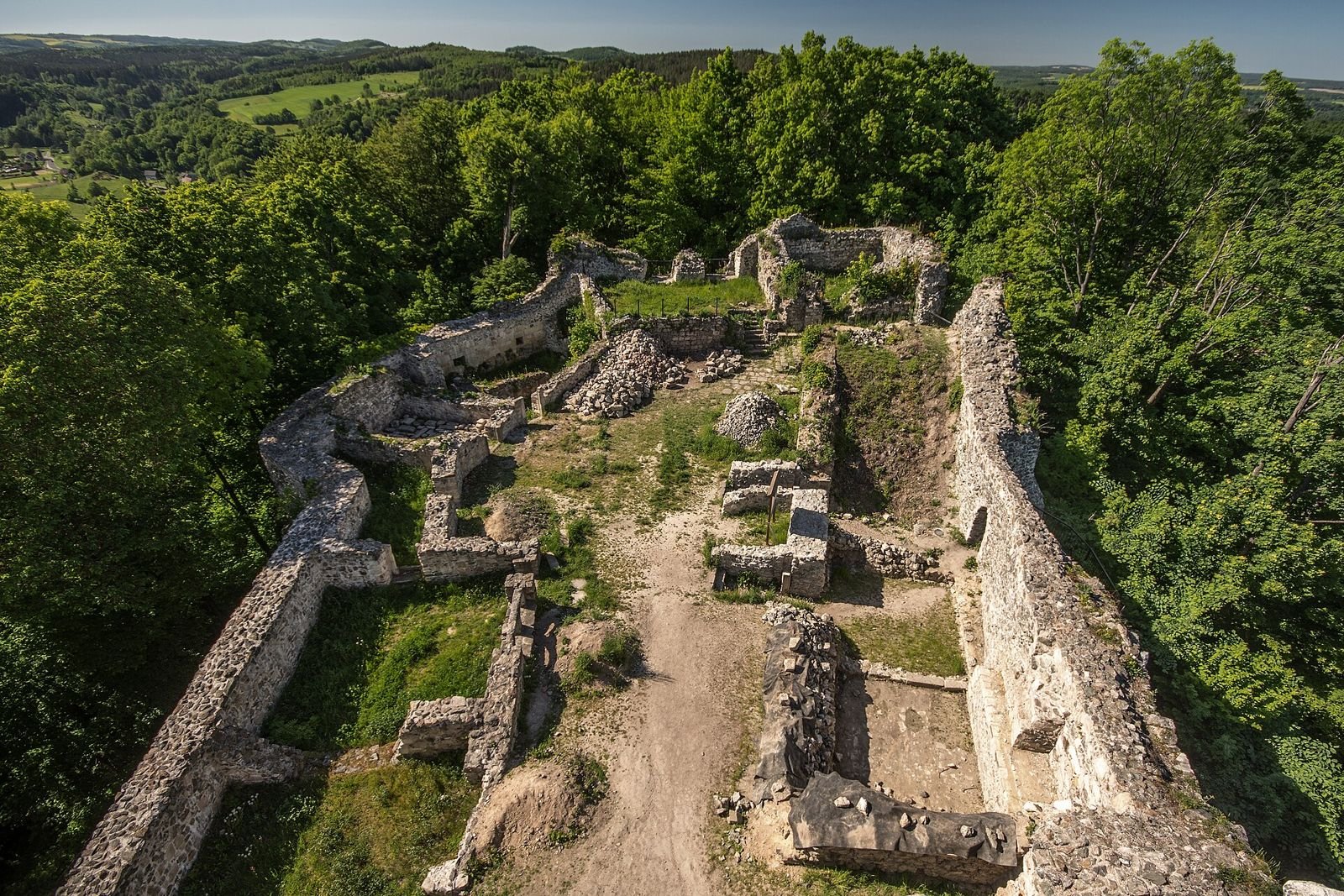 Widok z góry na ruiny murów zamku Wleń otoczone zielonym lasem, z trawiastym dziedzińcem pośrodku.